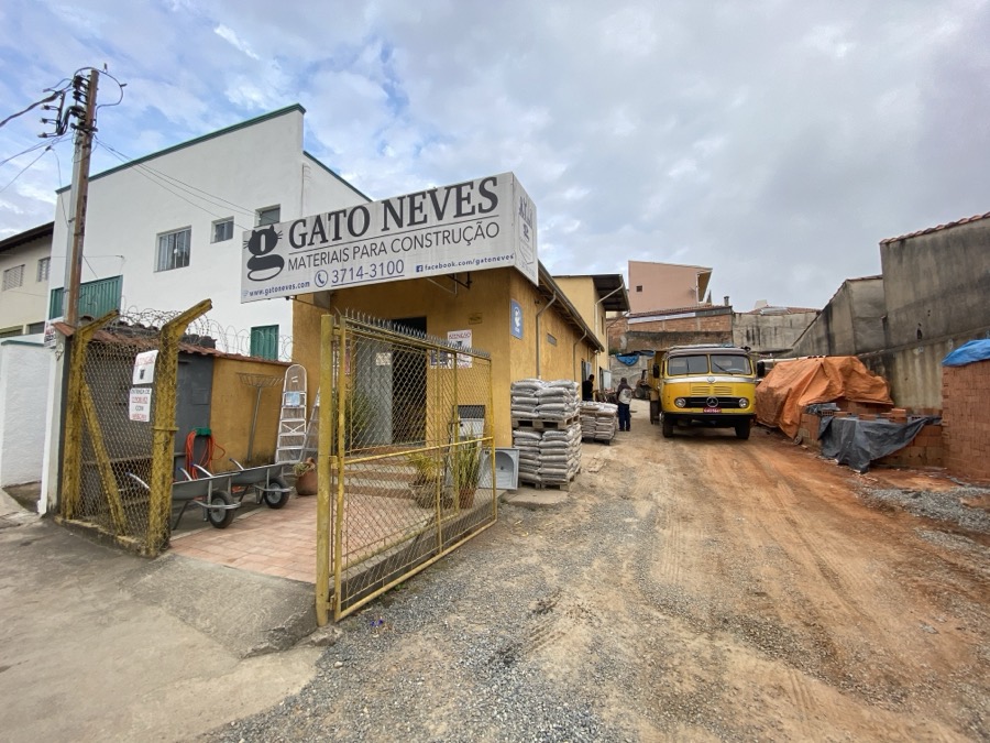 Fachada da Gato Neves Materiais para Construção, com placa branca, prédio amarelo e caminhão de entrega no pátio